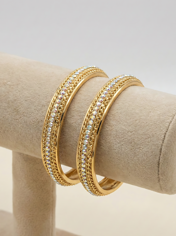 Lumina Luxe classic eternity-inspired bangles in a luminous golden-tone finish, featuring a continuous row of iridescent micro-crystals on a cream-colored jewelry display.