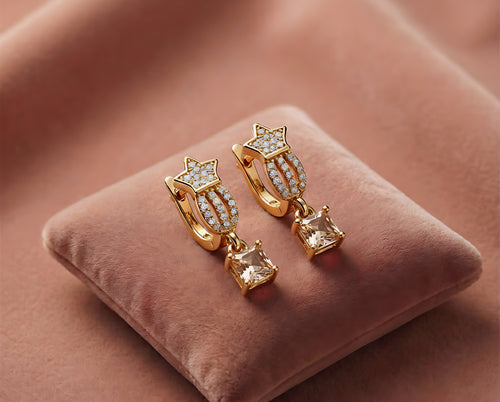 Gold earrings with star and gemstone designs on a pink velvet cushion