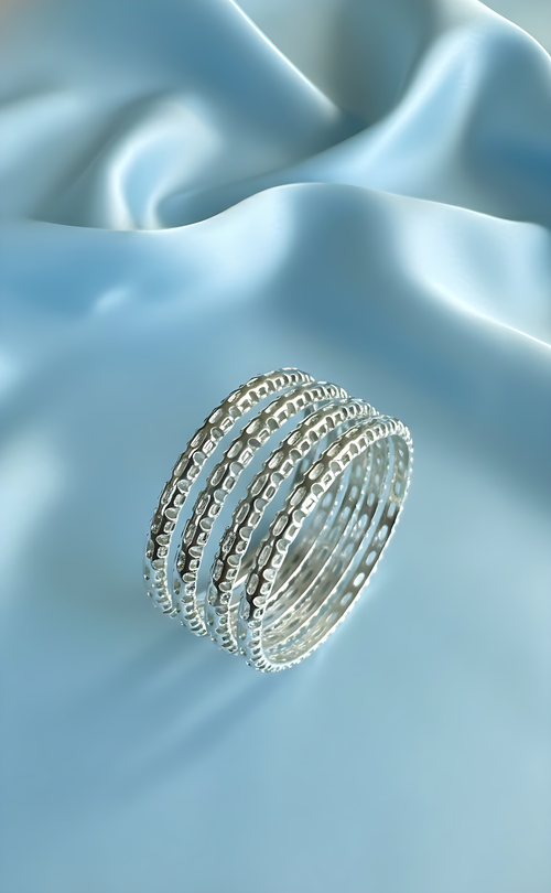 A set of five stackable bangles with a hammered texture in a [Luminous Gold / Radiant Silver] finish, displayed on a soft blue silk background.